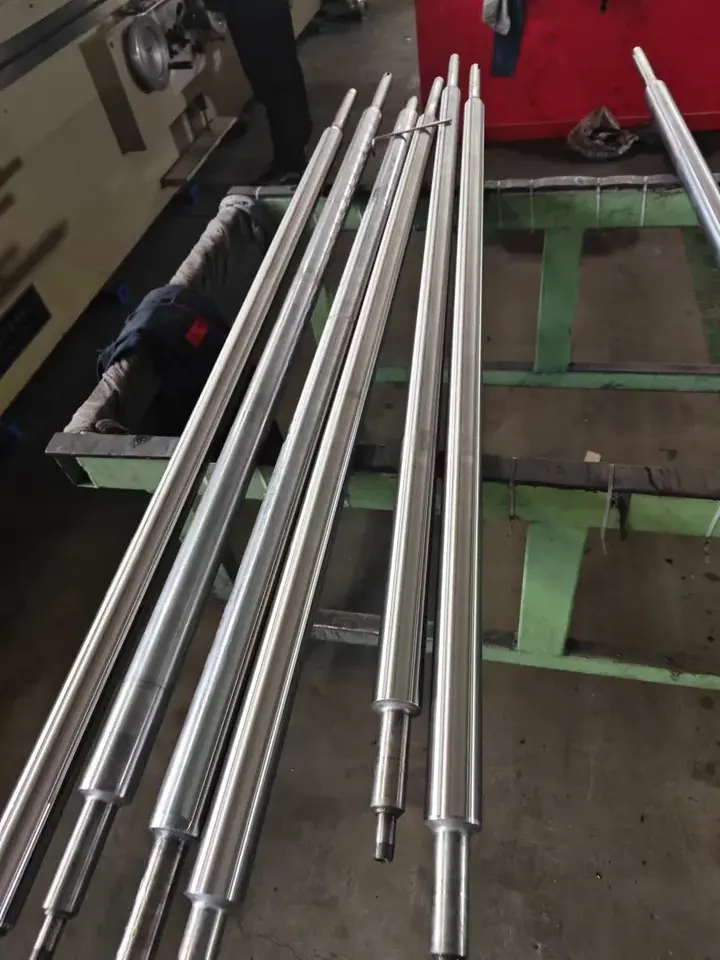Long machined leveling rolls photographed beside processing equipment